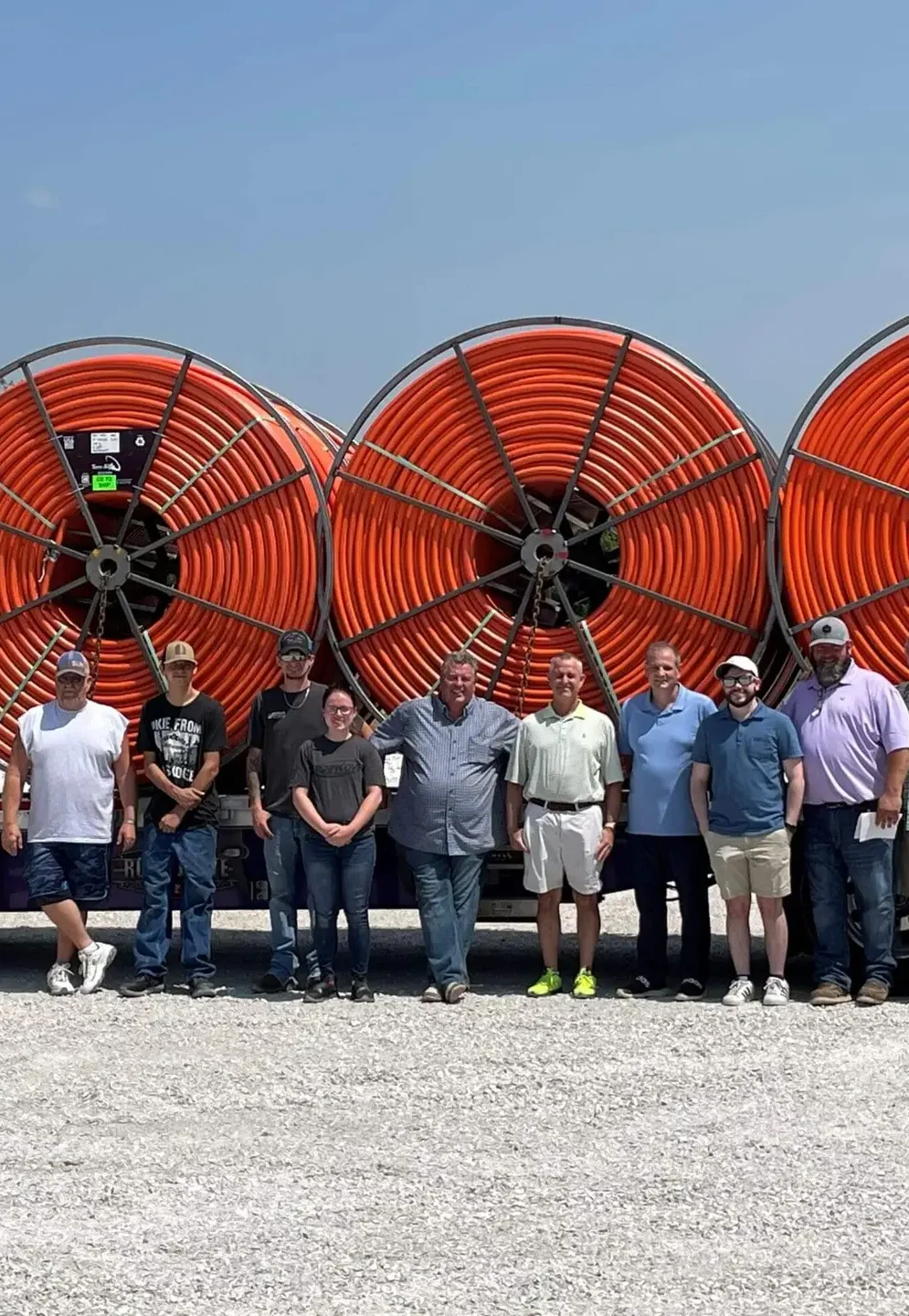A group photo of the Terra Star team outdoors in front of a truckbed loaded with orange 6" HDPE Conduit on reels