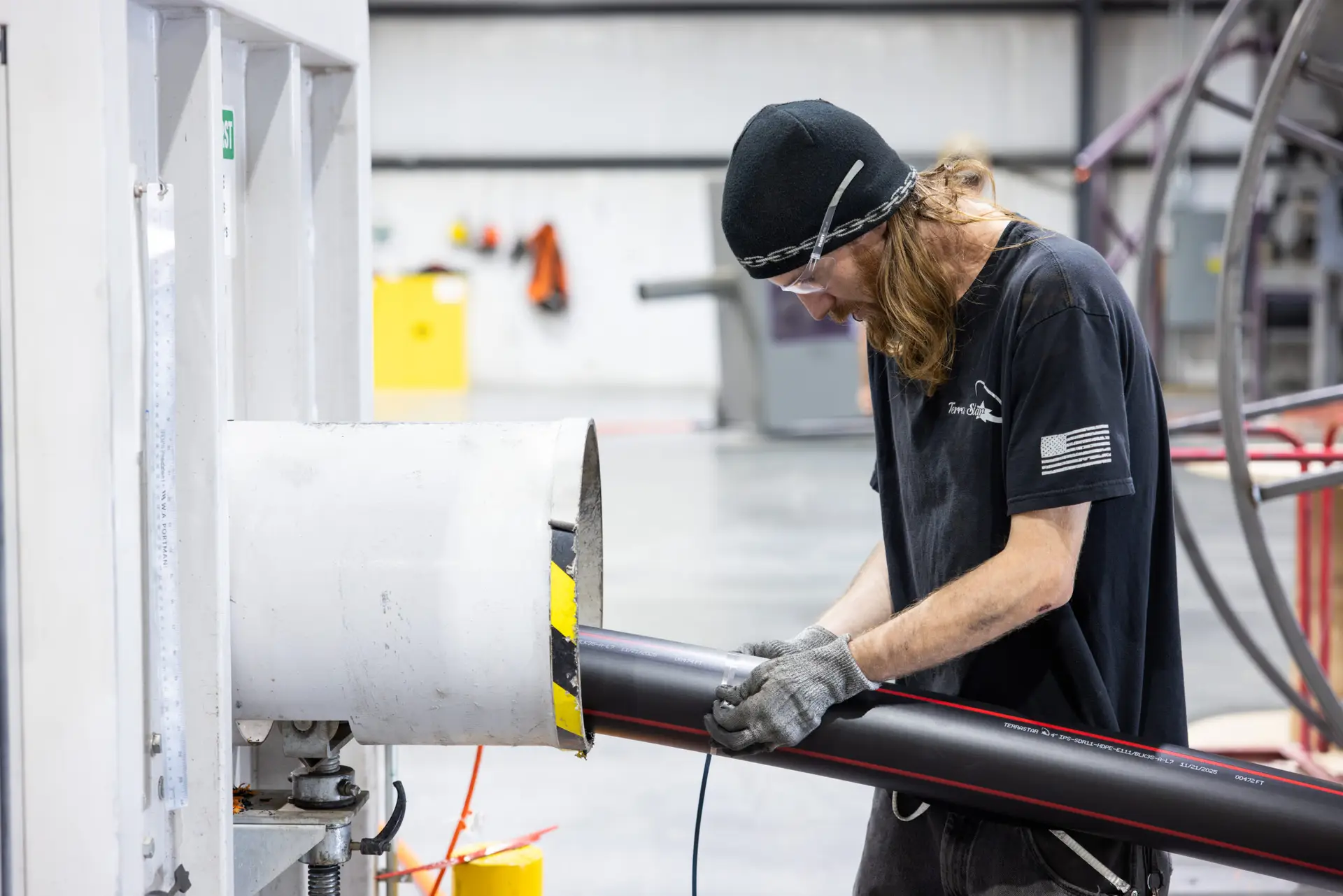 A Terra Star employee checks and refines the 6" HDPE (high-density polyethylene) conduit in black resin that is being extruded from the manufacturing line he is working on.
